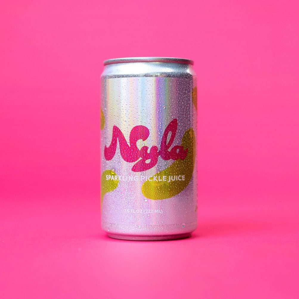 A silver aluminum can of Nylah soda with pink and yellow graphics, standing upright on a solid pink background.